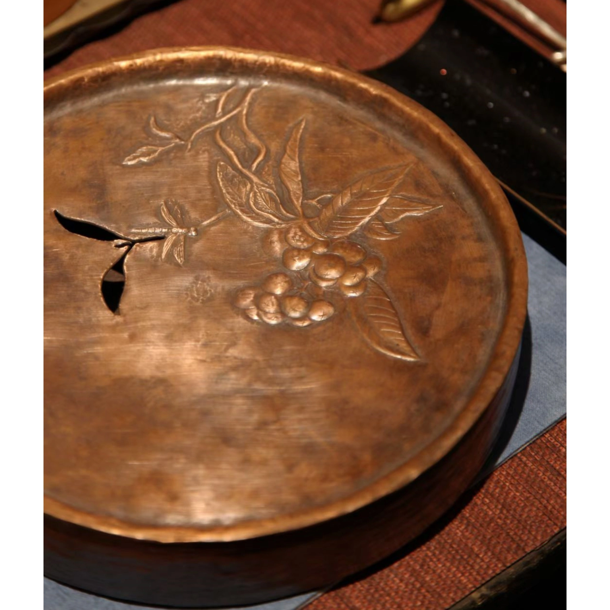 Close-up of hand-engraved pattern on copper teacup saucer, showing fine carving lines and hammered surface texture,
