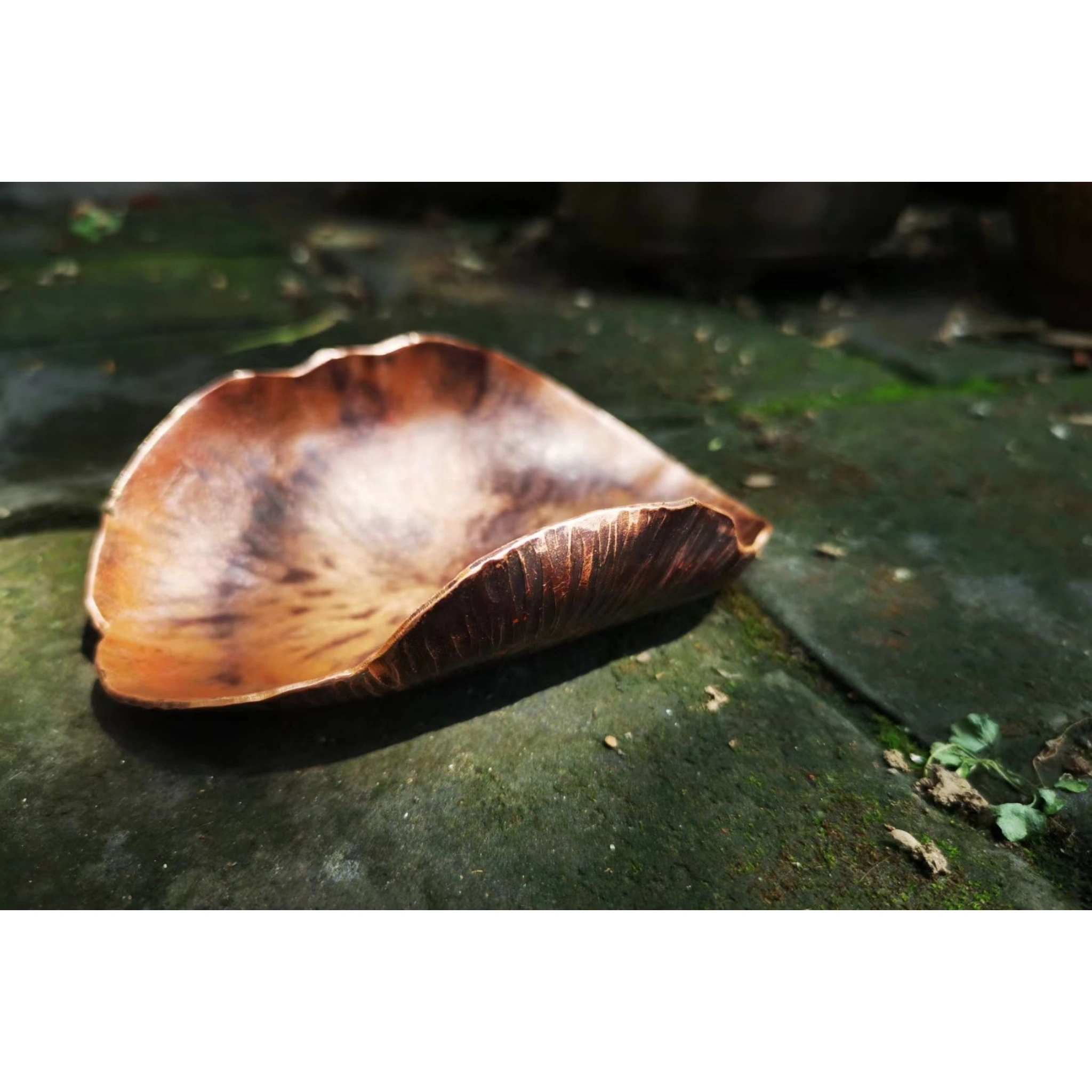 Hammered copper leaf-shaped tea scoop resting on moss-covered stone, natural texture contrast with oxidized patina,