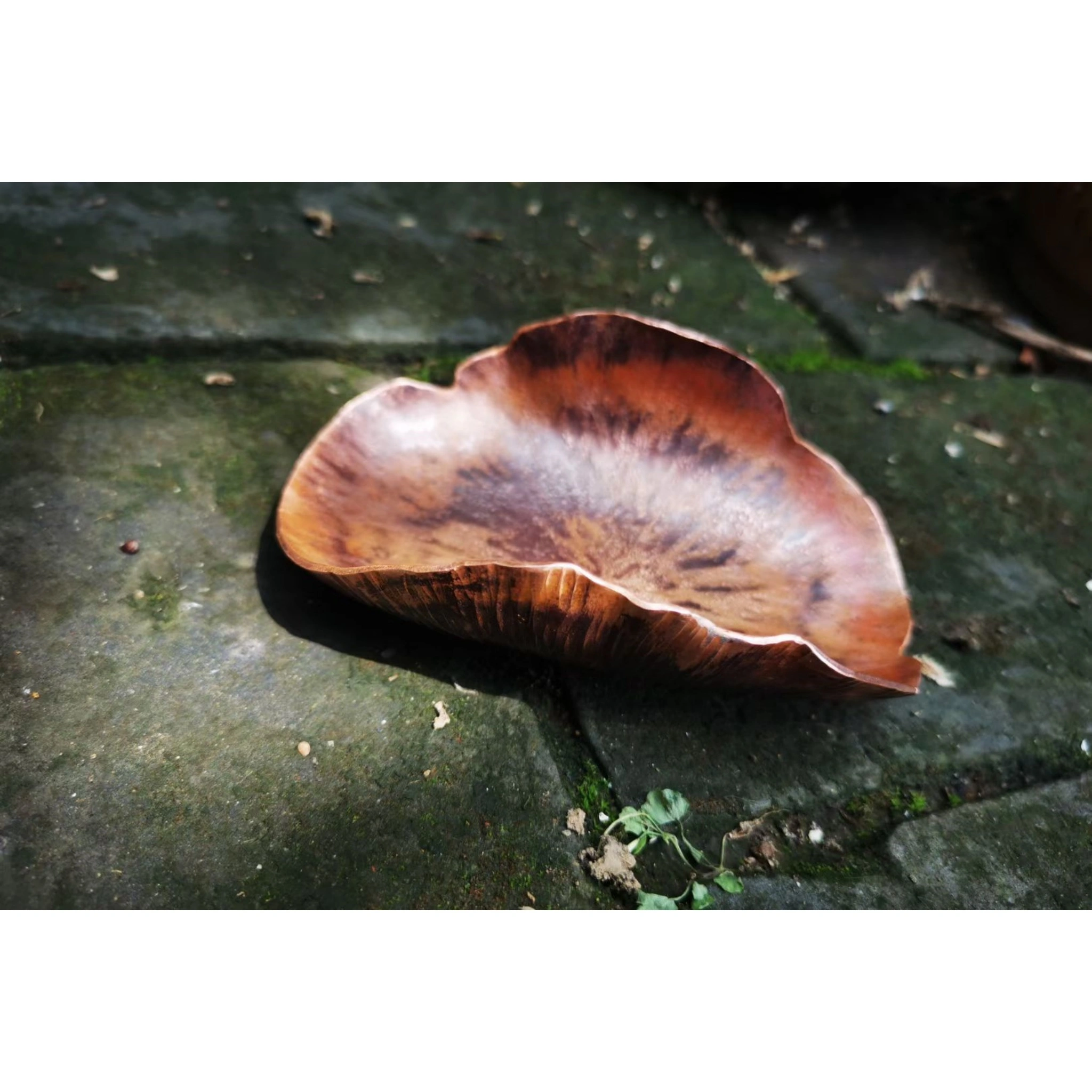 Close-up of hammered copper leaf tea scoop on mossy ground, highlighting copper patina and leaf vein details,