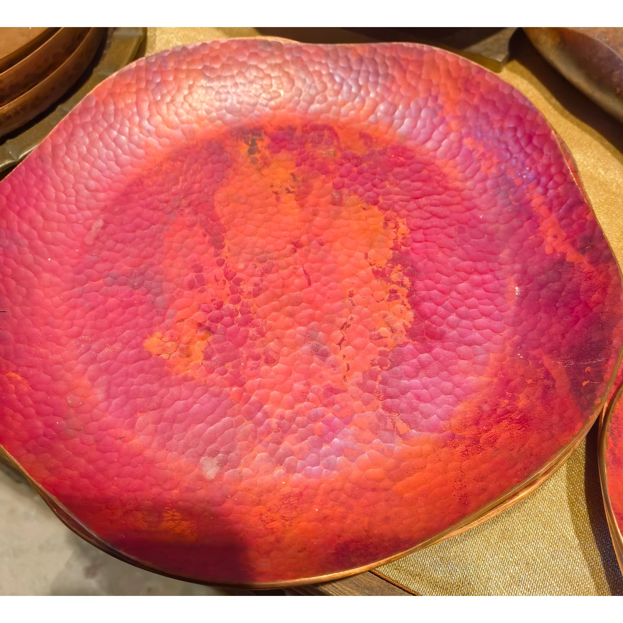 Front view of an oxidized copper teapot stand, highlighting the irregular hammered convex-concave texture and rustic patina,