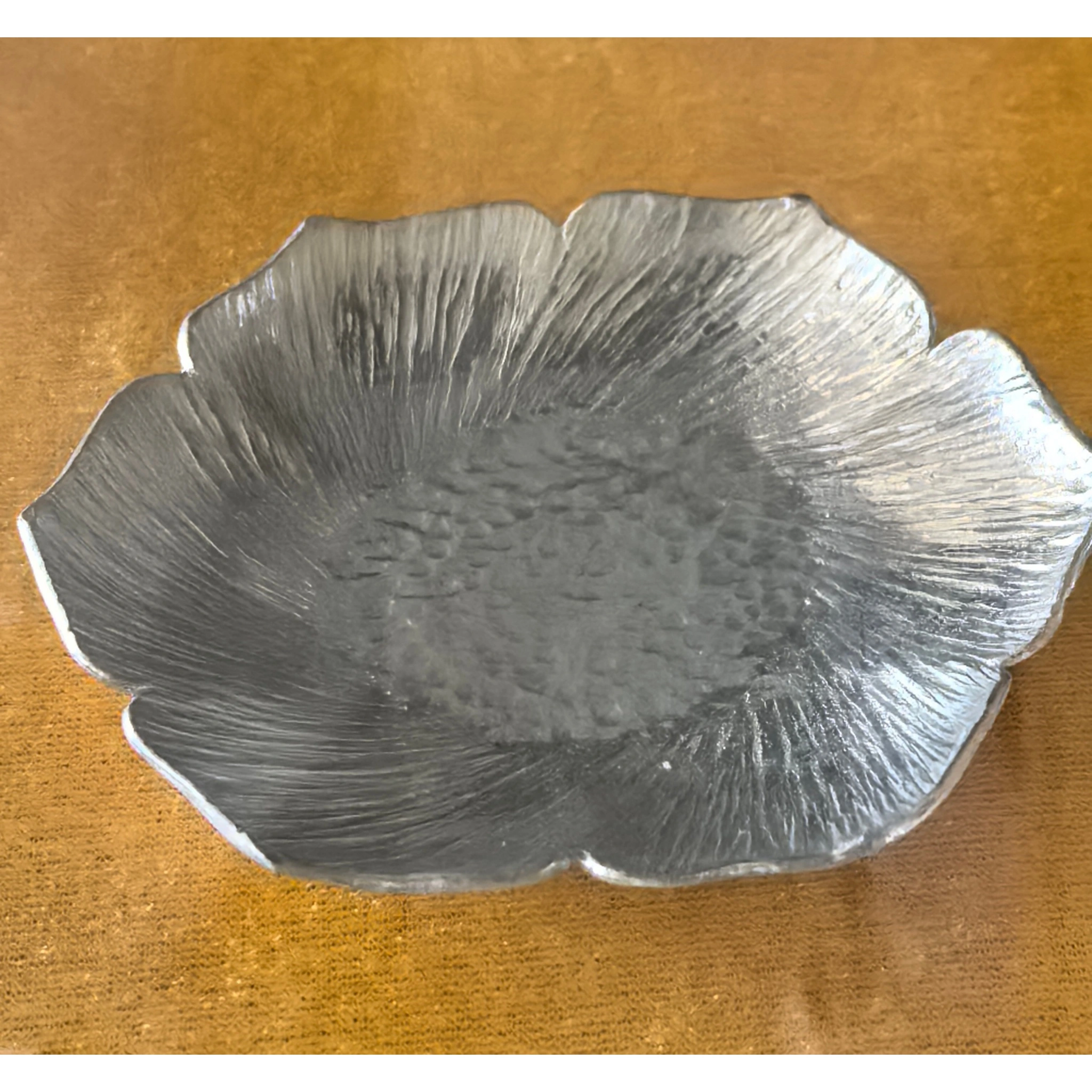 Hammered tin petal-shaped teapot stand from side angle, showing layered petal edges and metallic finish,