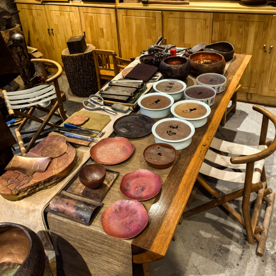 Collection display of hammered copper tea utensils featuring teapot stand and leaf-shaped tea scoop, finished metal artworks, by Heritage & Craft.