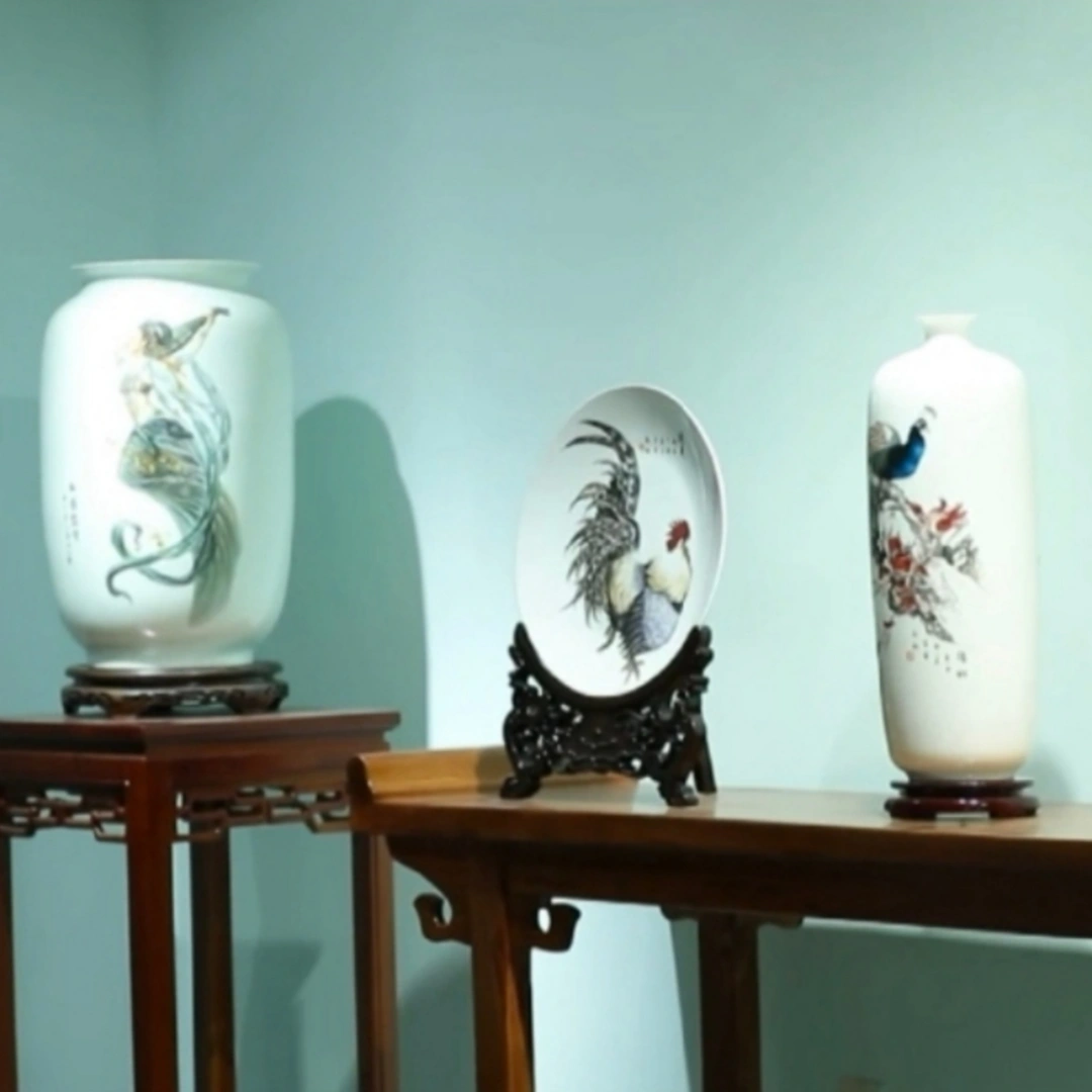 Collection display of hand-engraved porcelain artworks featuring carved plates and vases arranged in showcase setting, by Heritage & Craft.