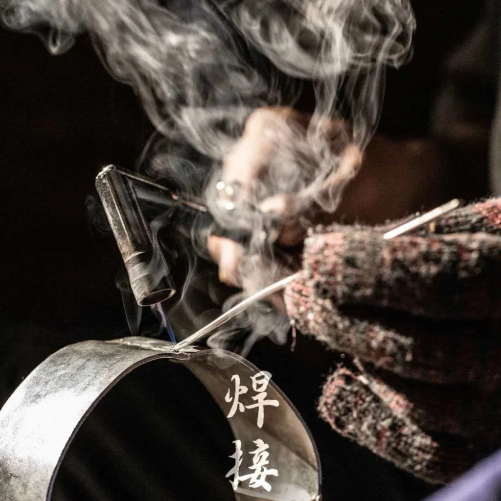 Tin carving artisan performing welding joint on metal surface with flame and solder, traditional Chinese tin craft, by Heritage & Craft.
